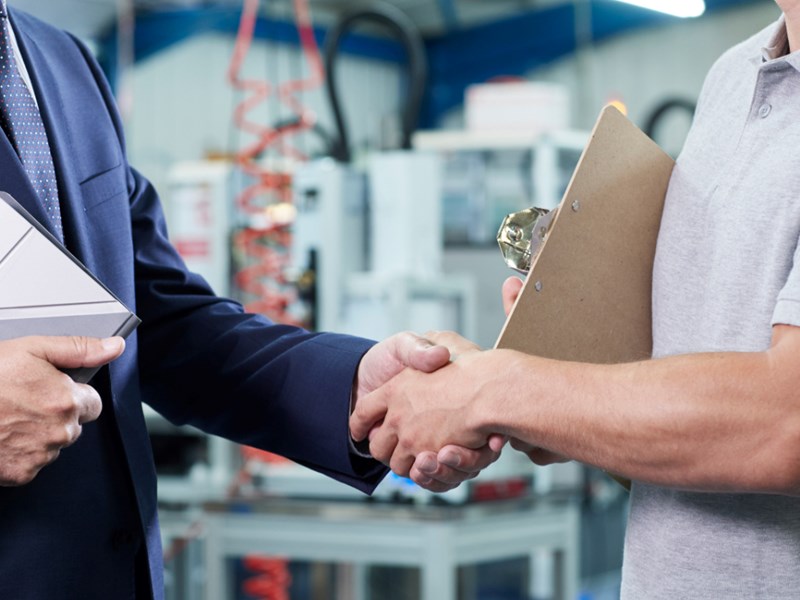 Close Up Of Business Owner With Digital Tablet In Factory Shaking Hands With Engineer